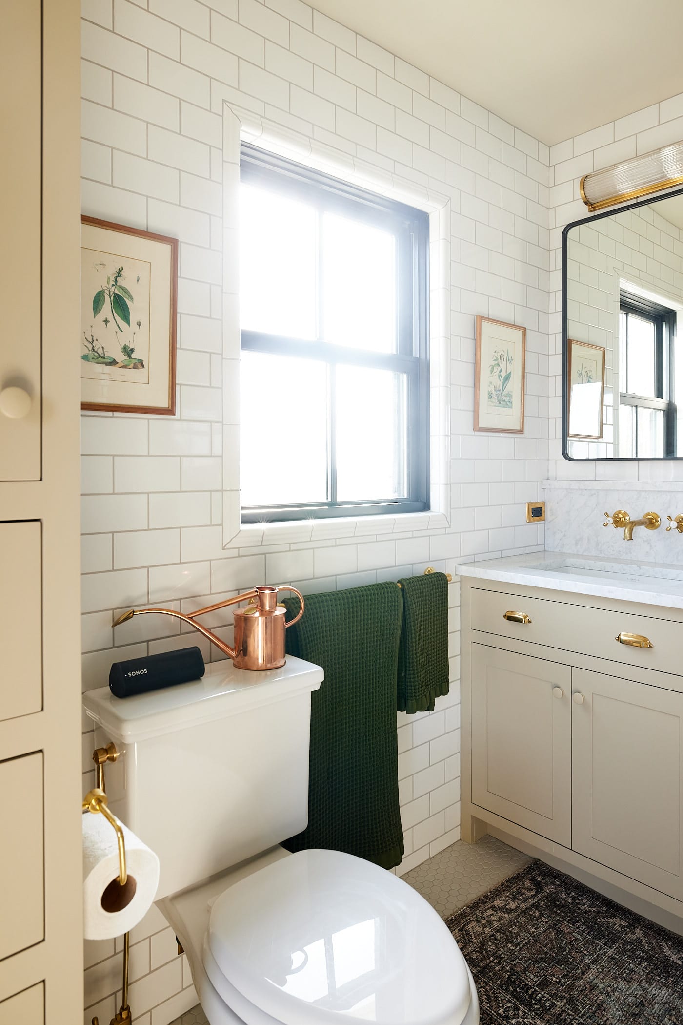 Window with lots of sunlight streaming in with toilet to the front and cabinet with sink to the side along with mirror in bathroom.