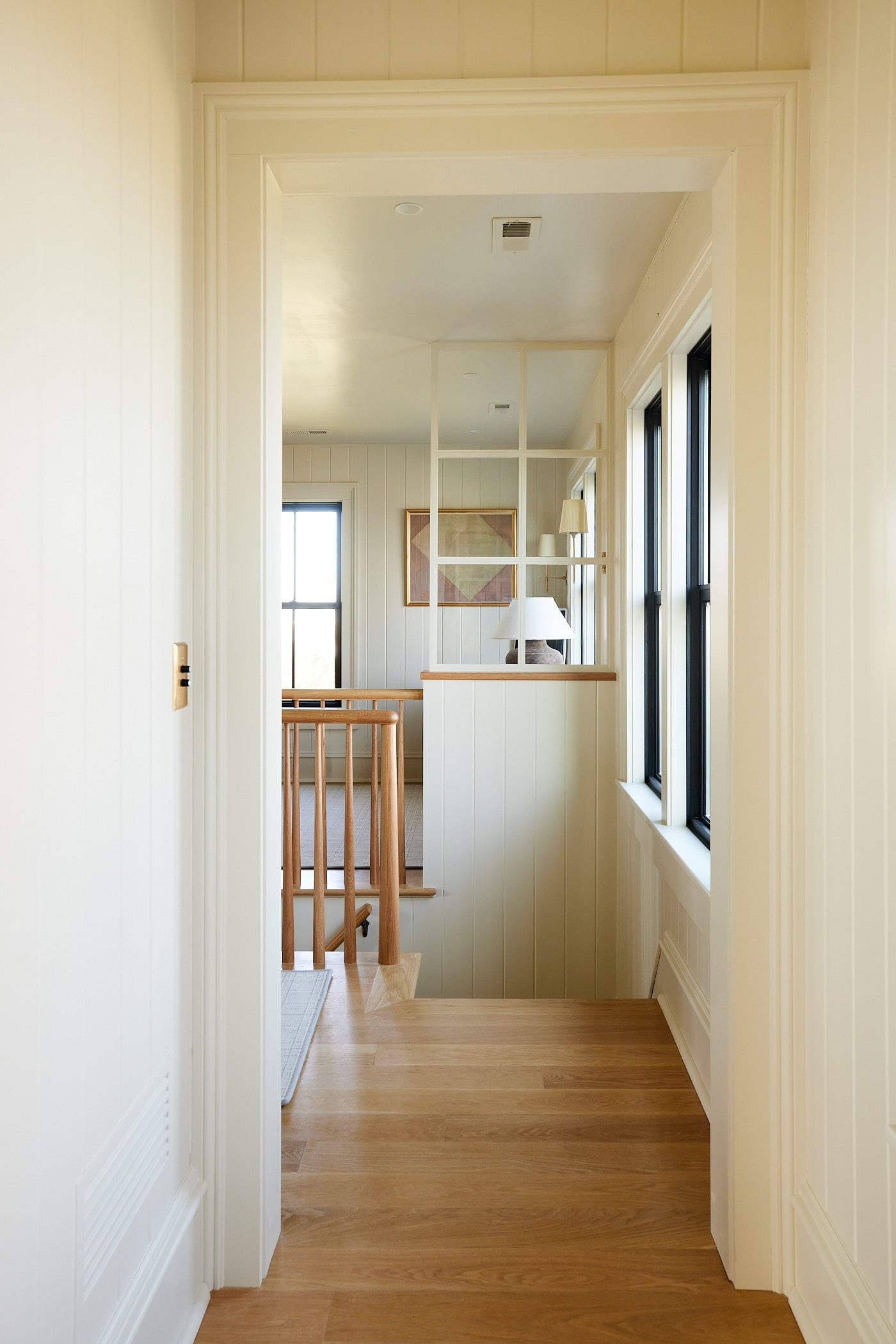 Stairwell with white oak floors with half wall on the far side with faux glass interior window separating the space.