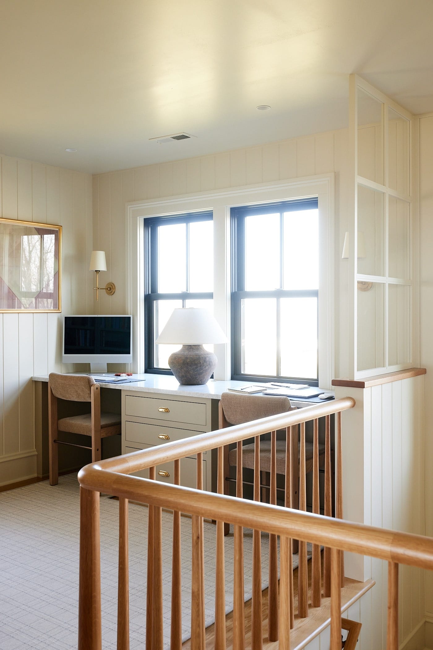 Upstairs office in farmhouse with two desk spaces in front of two large windows with white oak railing leading to downstairs.
