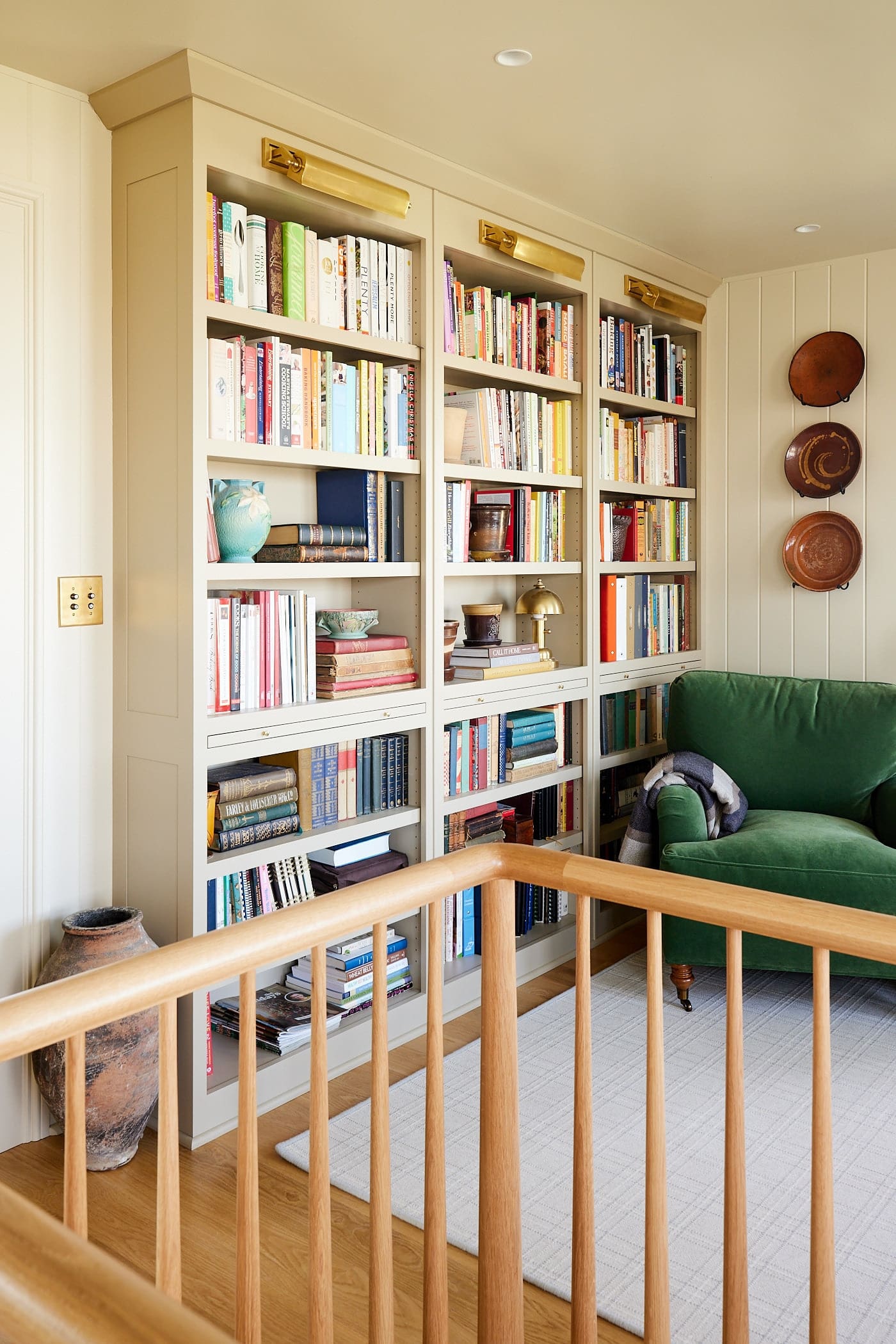 Three large bookcases with lots of cookbooks with green chair sitting to the side ready for reading with white oak rail running in front.