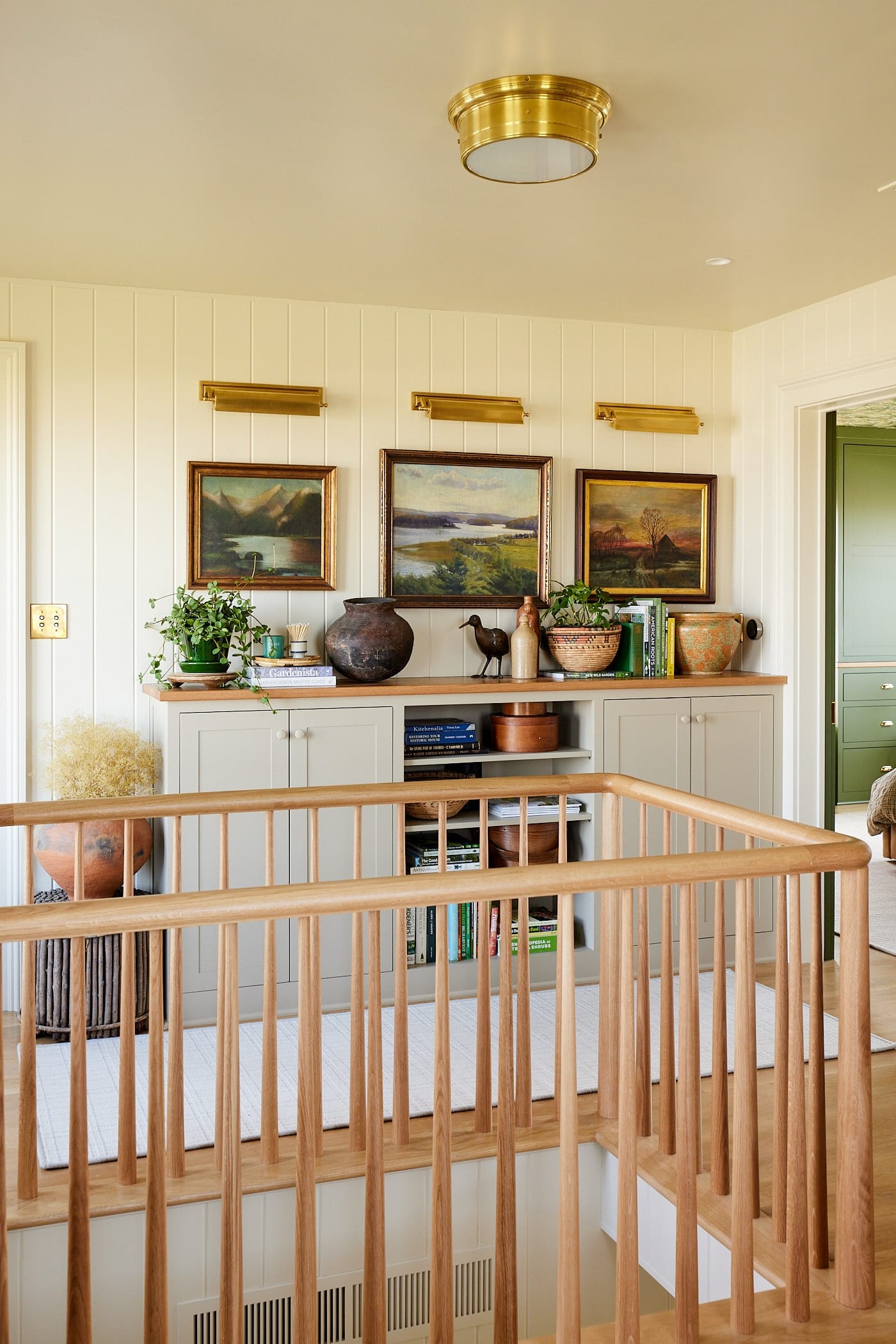 Built-in cabinet unit against one wall of an open hallway with display pieces on top and white oak railing surrounding the open stairwell.