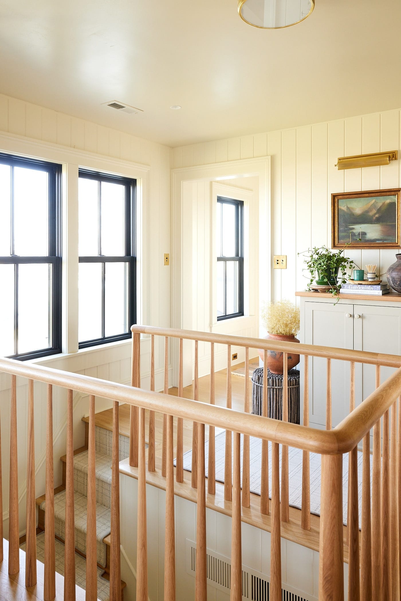 Wide open hallway at the top of a stairs with a white oak railing on three sides with built-in shelves on one side and windows to the north on the other.