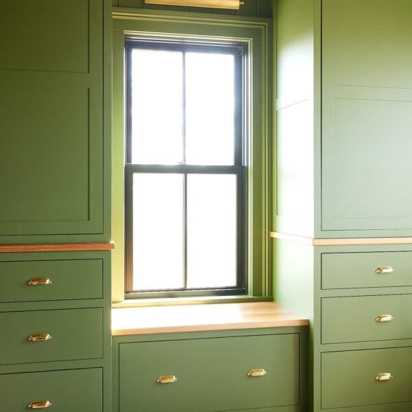 Cabinets painted a green color with a window and window seat in between with lots of light pouring in.