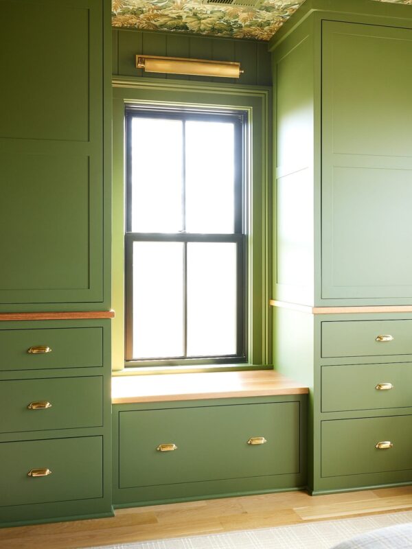 Cabinets painted a green color with a window and window seat in between with lots of light pouring in.