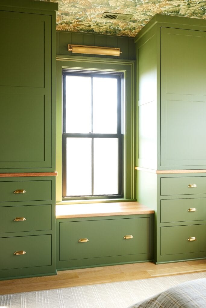 Cabinets painted a green color with a window and window seat in between with lots of light pouring in.
