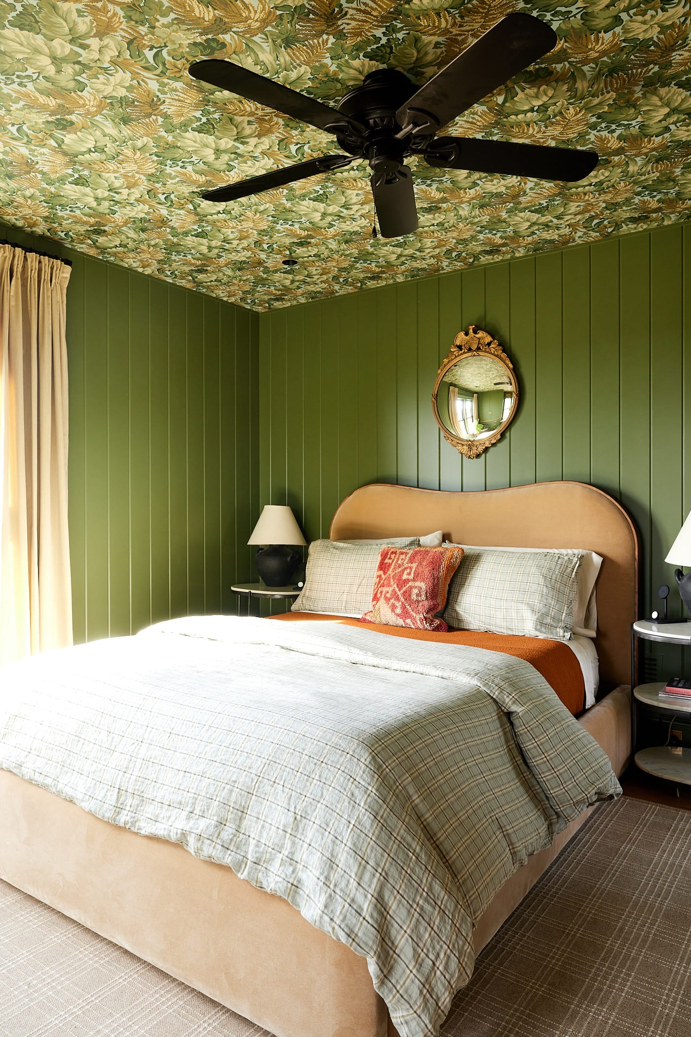 Large queen-size bed with pillows and orange comforter with green colored walls with side tables.
