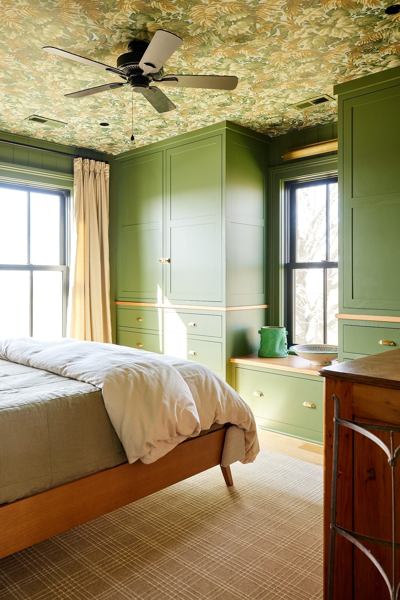 Bedroom with two built-in cabinets in green color with a window seat in between them and windows letting in lots of light.