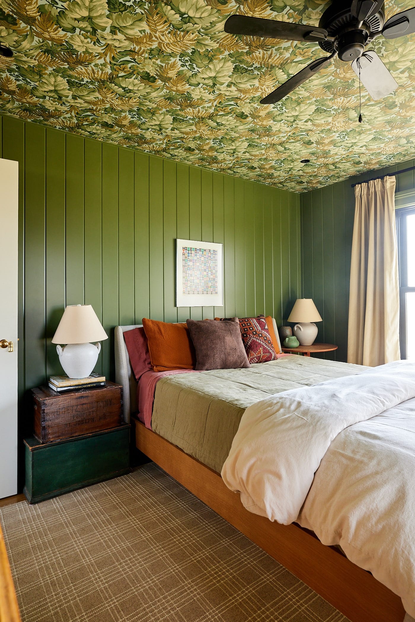 Queen-size bed with two side tables made from antiques with green colored walls and floral green wallpaper on the ceiling.
