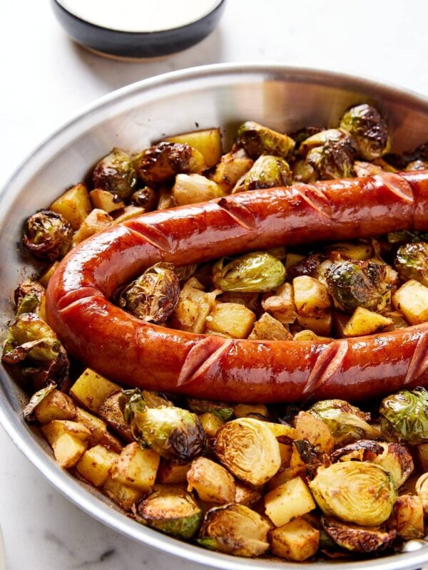 Metal skillet filled with cooked Brussels sprouts and potatoes with kielbasa on top.