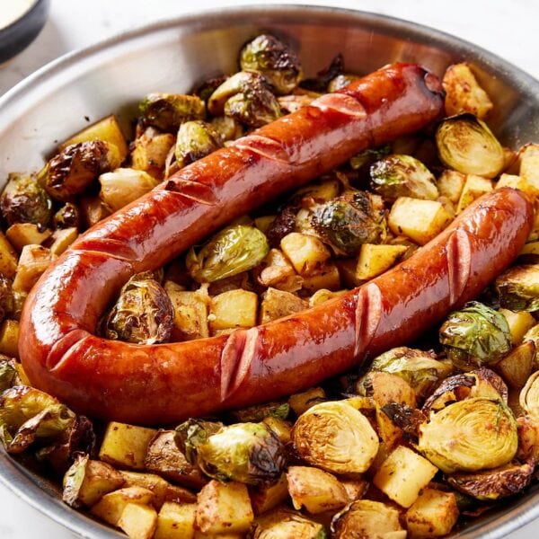Metal skillet filled with cooked Brussels sprouts and diced potatoes with browned kielbasa on top.