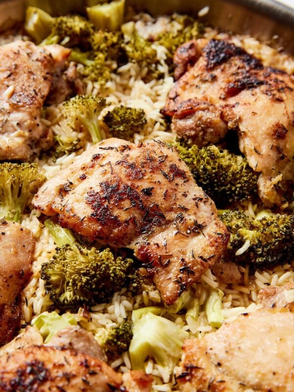 Chicken thighs cooked with rice and broccoli in a metal skillet right after coming out of the oven with crispy texture.