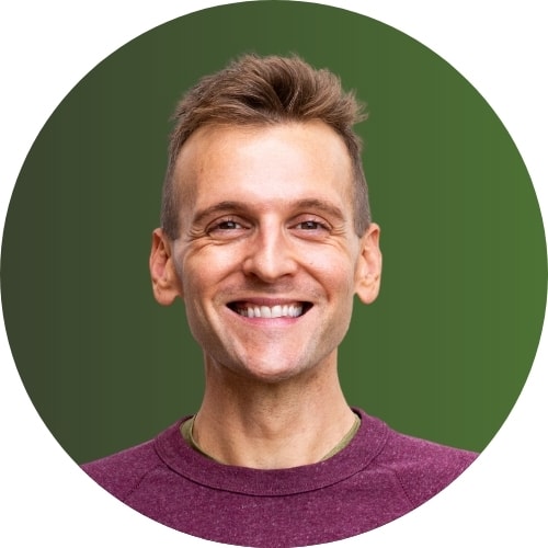 Kaleb Wyse wearing purple sweatshirt standing in front of green background while smiling.