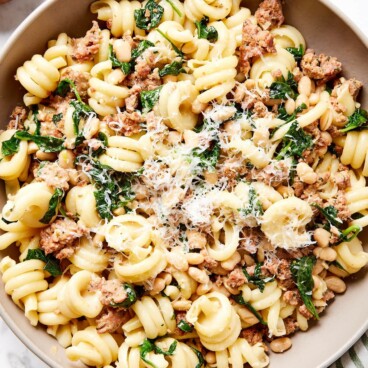 Brown bowl on marble surface filled with weeknight spinach and sausage pasta with Parmesan cheese sprinkled on top.