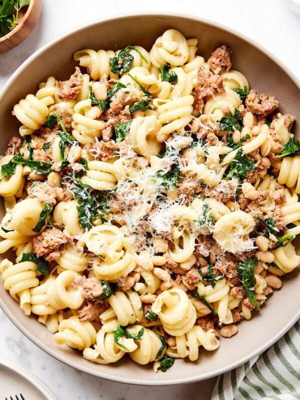 Brown bowl on marble surface filled with weeknight spinach and sausage pasta with Parmesan cheese sprinkled on top.