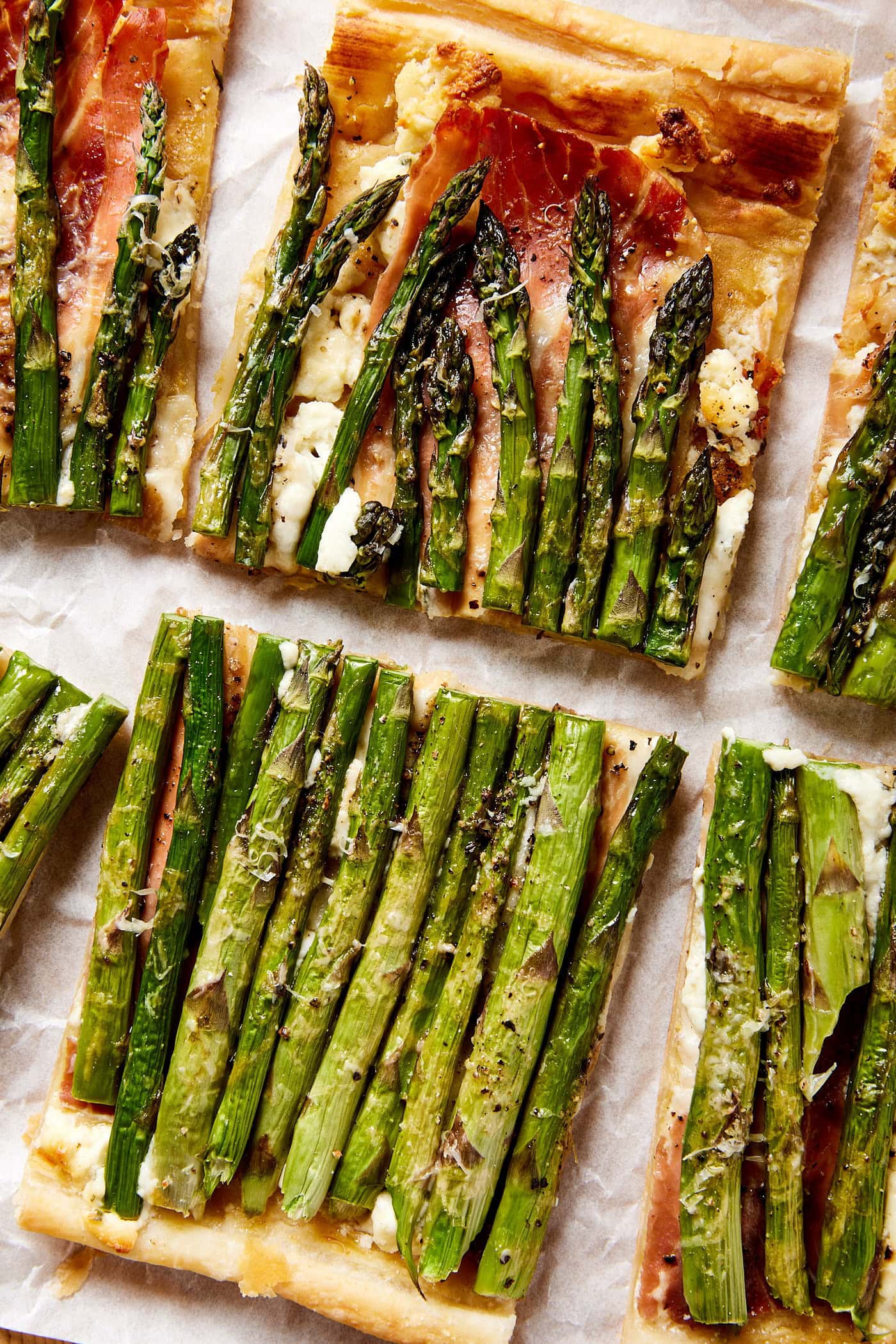 Baked asparagus tart sliced into squares with prosciutto underneath with piece of parchment paper.