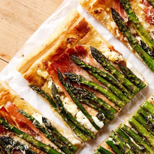 Squares of asparagus tart sitting on piece of white parchment on wooden board after being sliced.