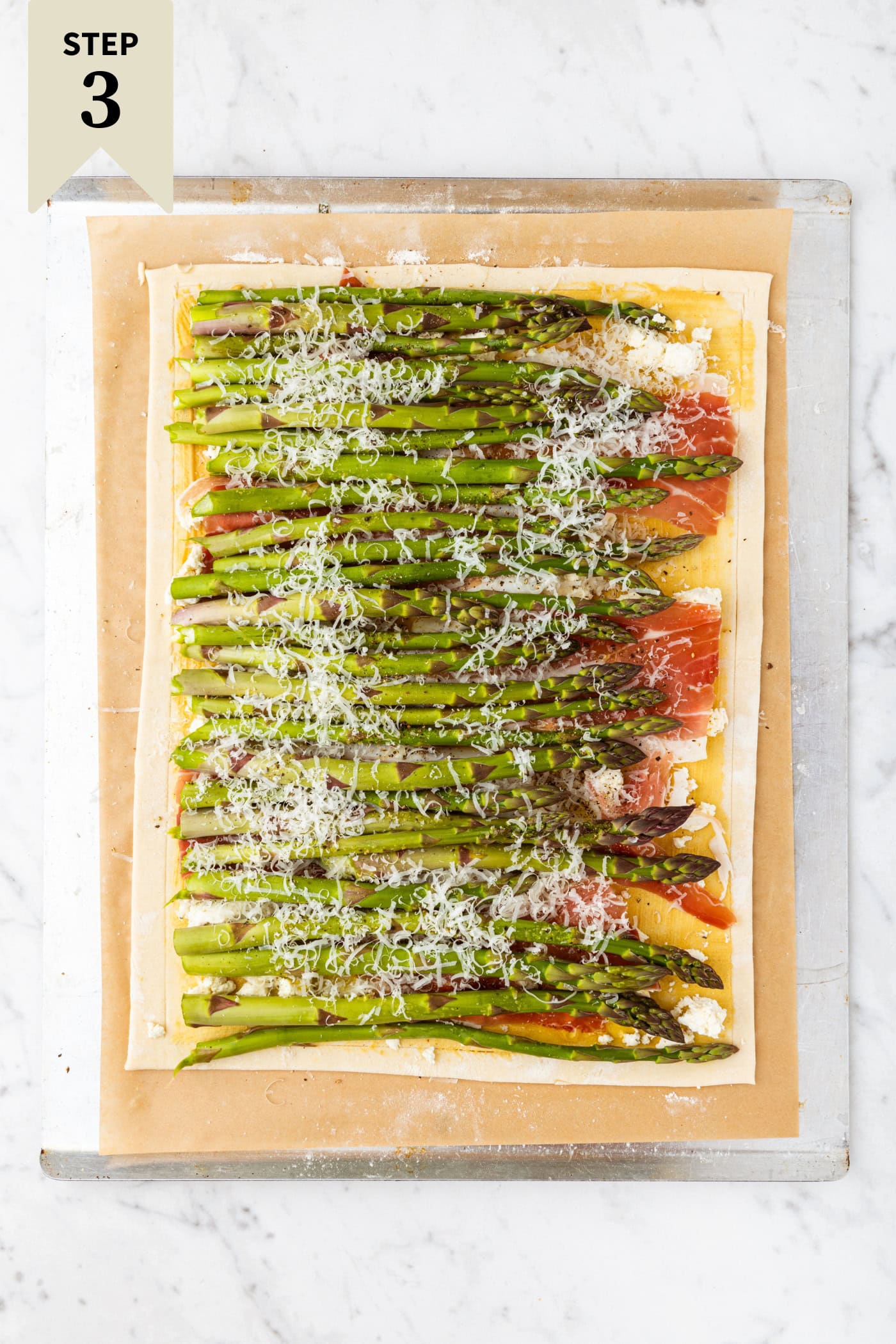 Asparagus tart with asparagus lined up on top of prosciutto and puff pastry topped with Parmesan cheese before going into the oven.