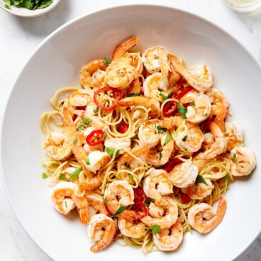 Large white bowl filled with garlic shrimp pasta with red peppers all on white marble surface.