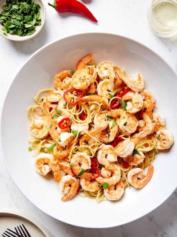 Large white bowl filled with garlic shrimp pasta with red peppers all on white marble surface.