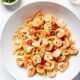 Large white bowl filled with garlic shrimp pasta with red peppers all on white marble surface.