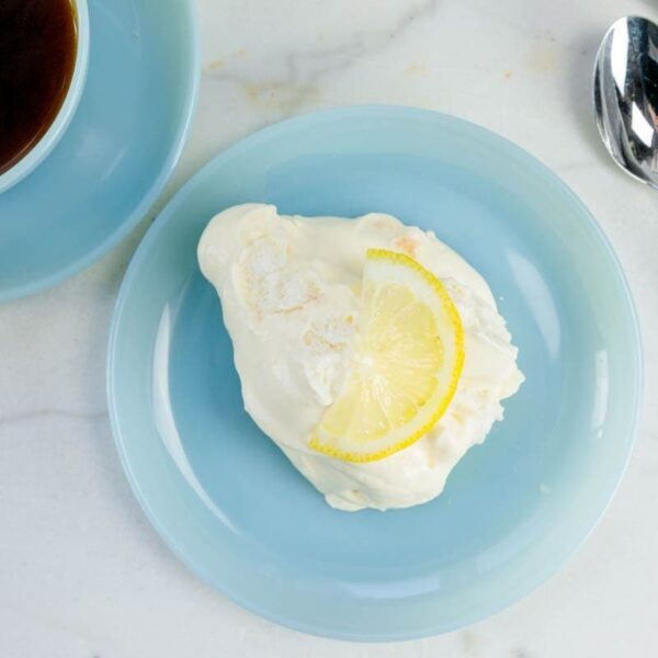 Blue plate with lemon pudding soufflé with slice of lemon on top with cup of coffee to the side.