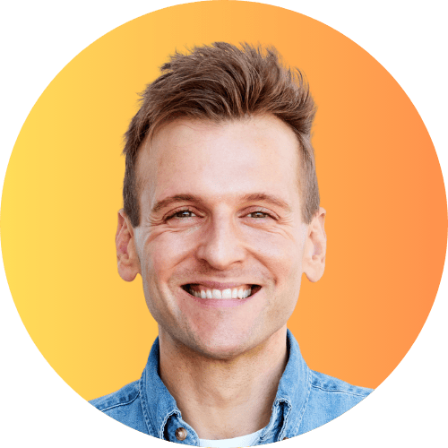 Kaleb Wyse standing in front of yellow and orange ombre background in a blue denim shirt.