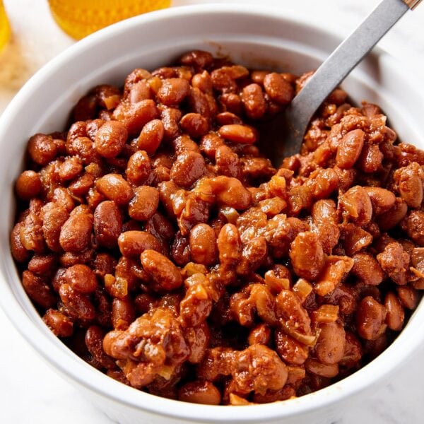 White serving dish filled with bbq baked beans with spoon resting in container ready for serving.