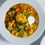 White bowl filled with slow cooker cauliflower curry soup with dollop of yogurt and sprinkling of parsley on top.
