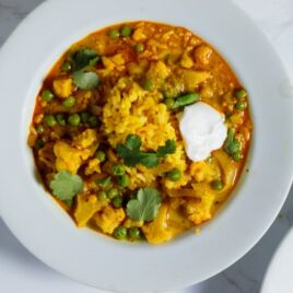 White bowl filled with slow cooker cauliflower curry soup with dollop of yogurt and sprinkling of parsley on top.