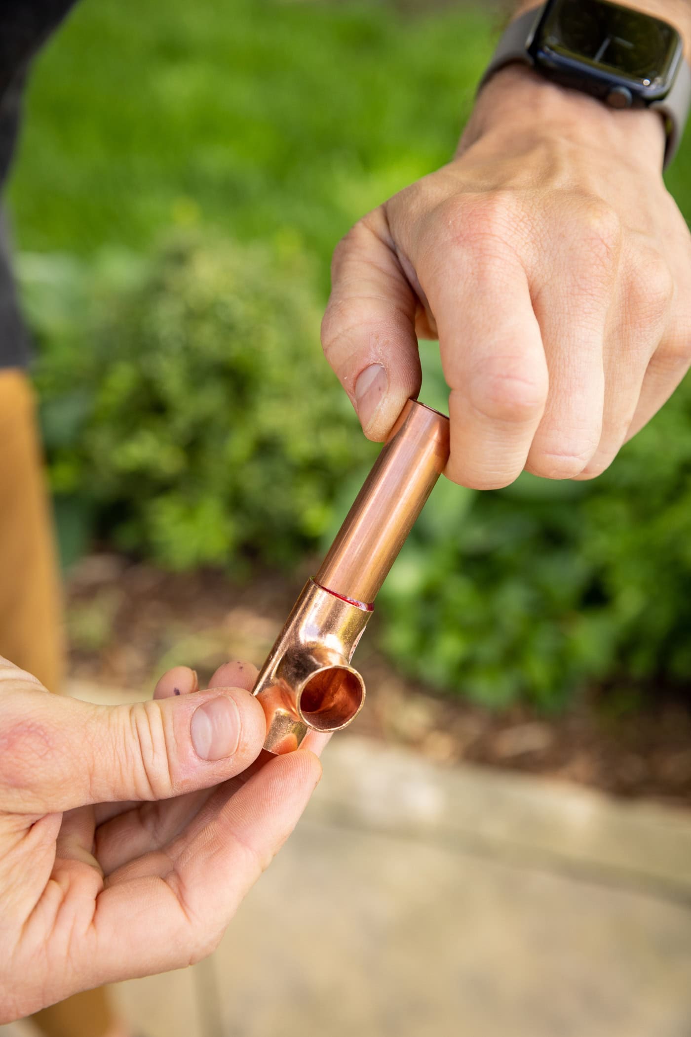 Hand showing a T fitting of a copper pipe for a DIY water fountain.