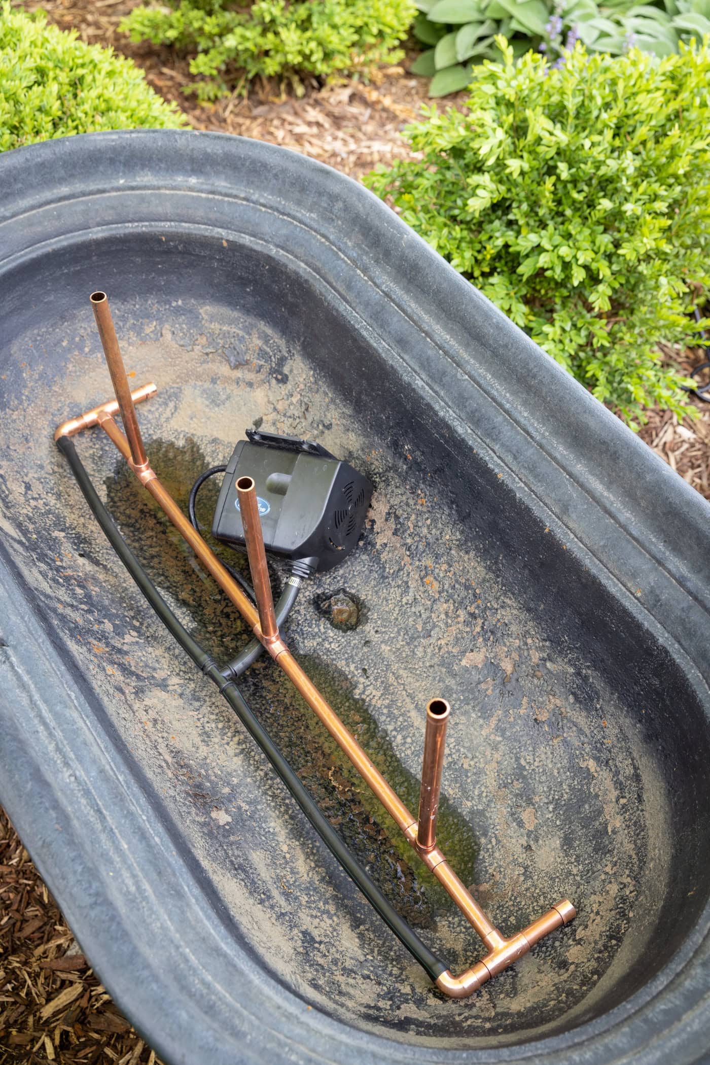 Copper pipe with a water pump attached to form a water fountain in a black cast iron trough.