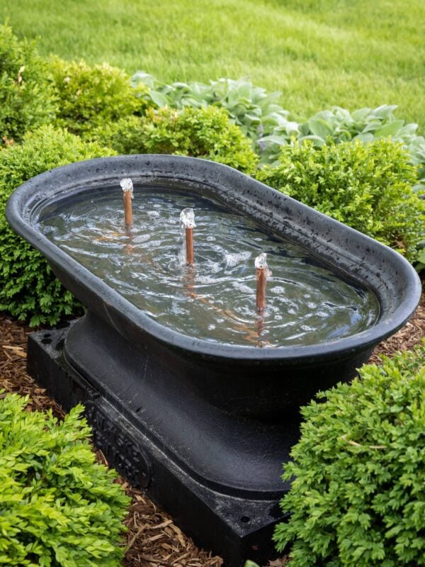 Black cast iron water fountain with copper bubblers with boxwood all around.
