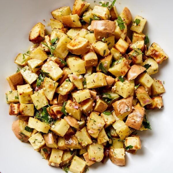 White bowl filled with diced sweet potatoes covered in mustard vinaigrette for a French potato salad.