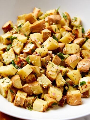 White bowl filled with French potato salad with herbs and whole-grain mustard seeds on top.