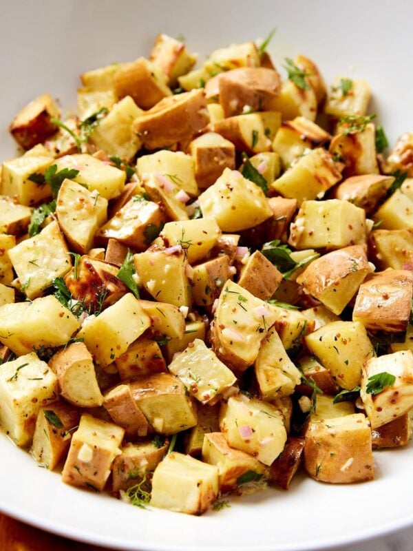 White bowl filled with French potato salad with herbs and whole-grain mustard seeds on top.