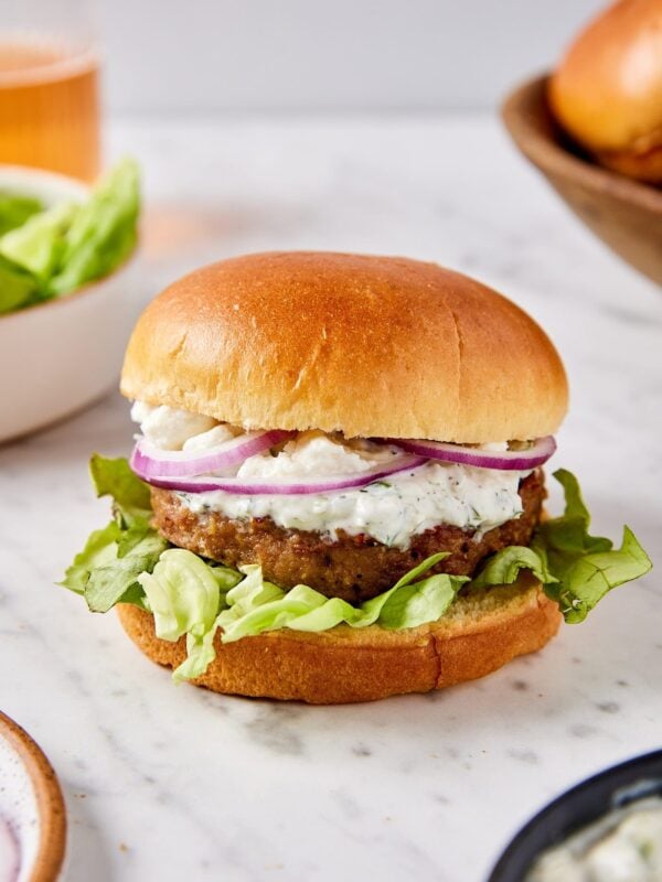Assembled turkey burger with homemade tzatziki sauce, lettuce, red onions, and crumbled feta cheese on top.