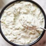Black bowl filled with tzatziki sauce with spoon scooping out a serving.