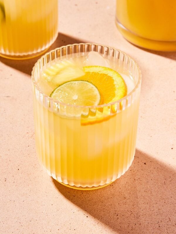 Glass filled with yellow-colored pineapple tequila sangria with lime and orange slices on top.