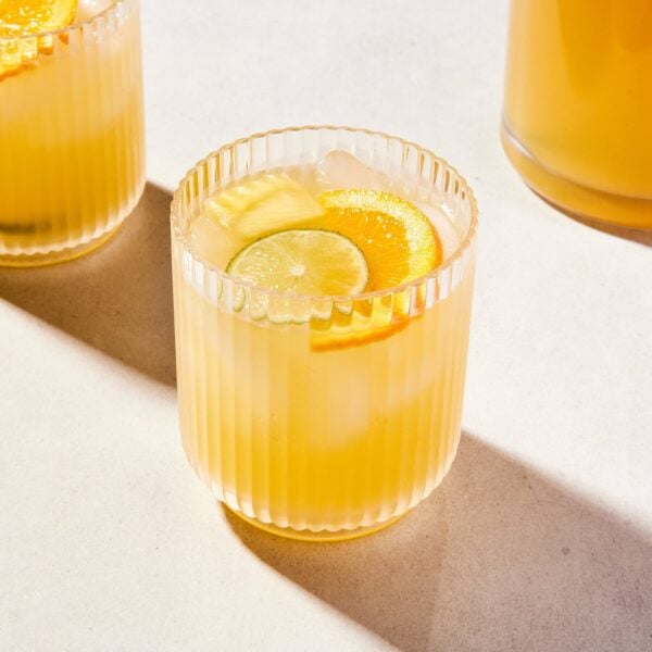 Glass of pineapple sangria with another glass behind as well as a pitcher.