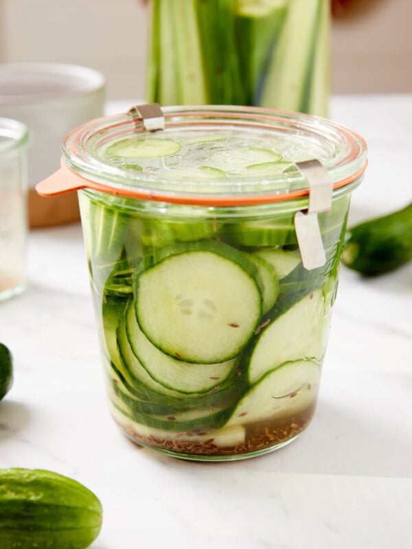 Glass jar filled with refrigerator dill pickles with dill seeds and brine all around pickles all on white surface.