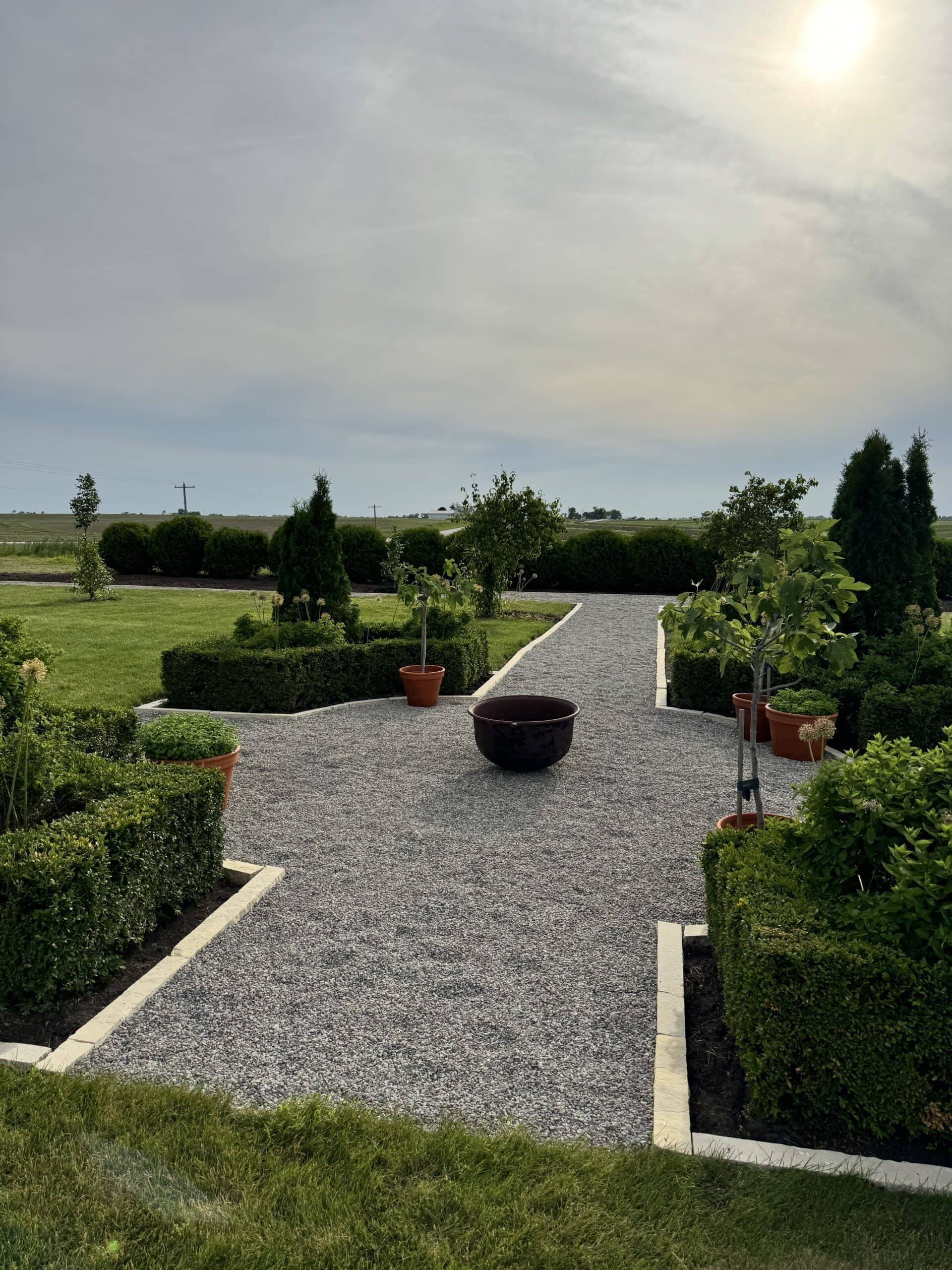 Fire pit with gravel and edging all around with boxwood and other plants.