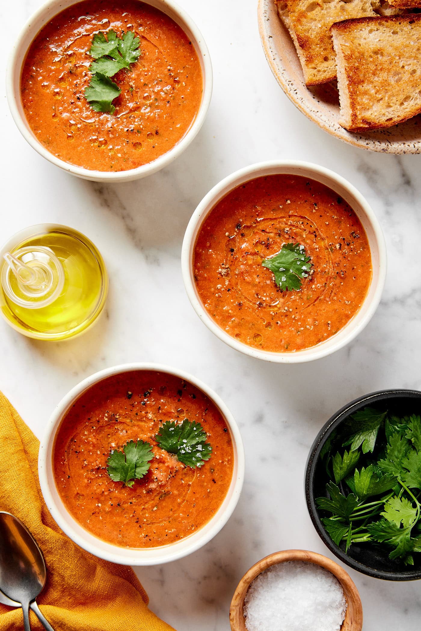 Three white bowls on marble surface filled with gazpacho soup with parsley on top.