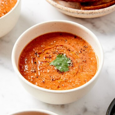 White bowl filled with easy gazpacho soup with olive oil, salt, and parsley leaf on top.