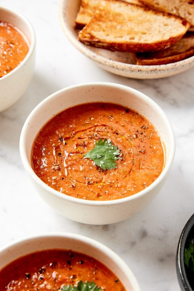 White bowl filled with easy gazpacho soup with olive oil, salt, and parsley leaf on top.