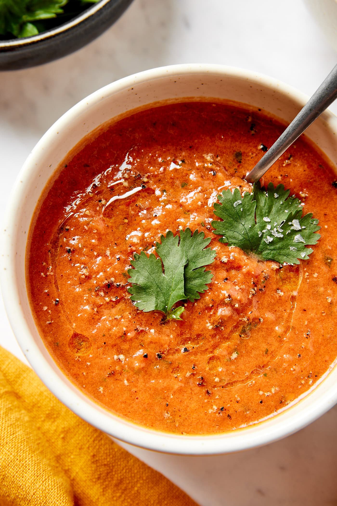 White bowl filled with creamy tomato soup with olive oil, black pepper, salt, and parsley sprinkled on top.