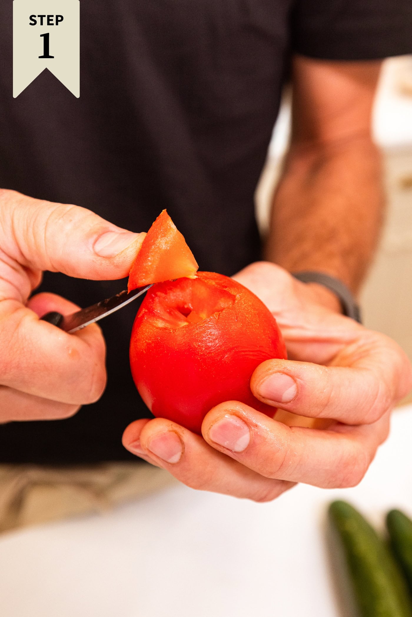 Hand using knife to cut out the core of a tomato before cutting into pieces.