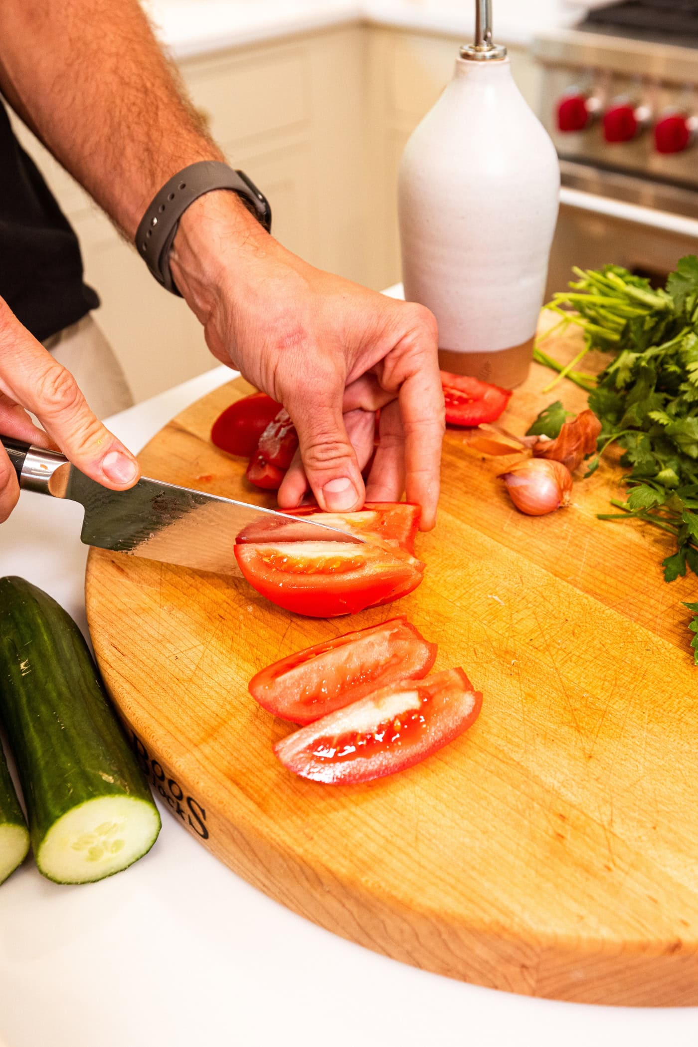 Hand using knife to slice a tomato into pieces on a wooden cutting board.