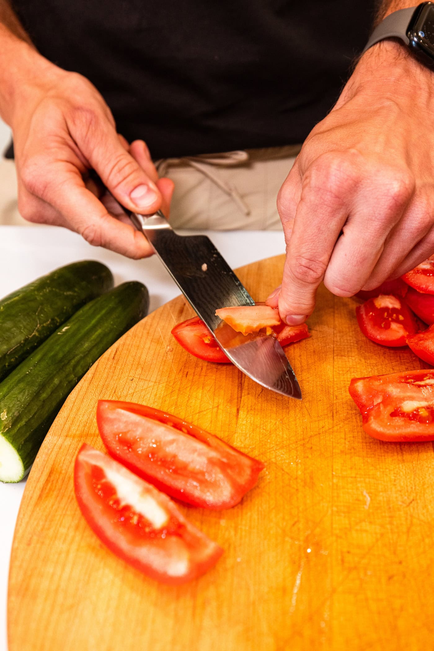 Hands using knife to slice off the white part of tomato sliced into quarters.