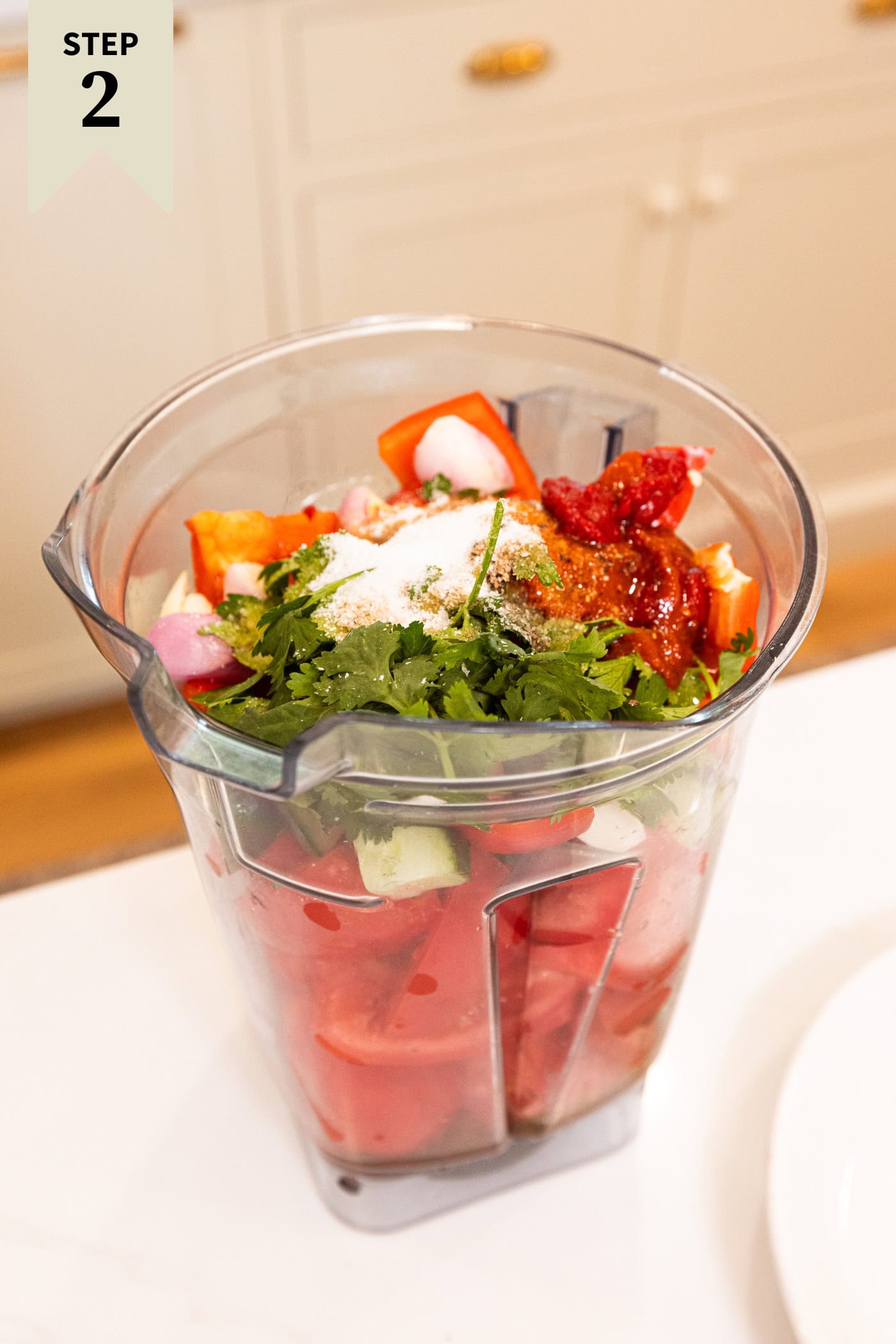 Blender filled with ingredients needed to make gazpacho including tomatoes, herbs, peppers, spices, and more.