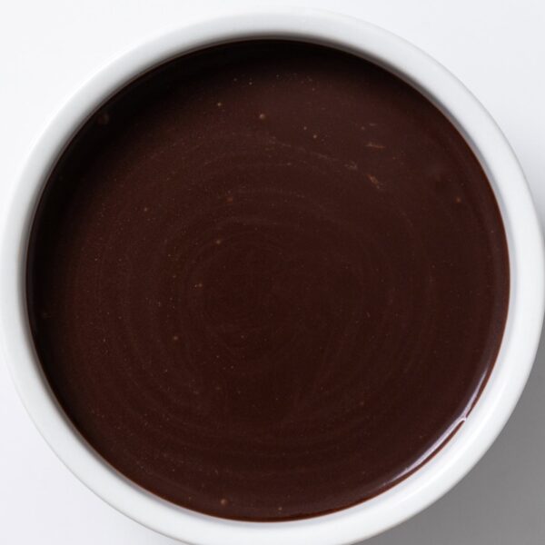 White bowl filled with hot fudge sauce on white surface.